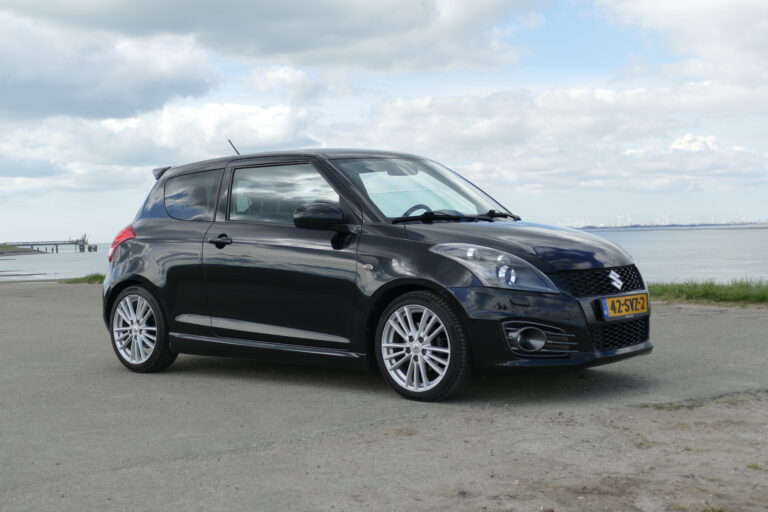 Zwarte Suzuki Swift Sport geparkeerd aan het water, voorzien van sportieve velgen en aerodynamische details.