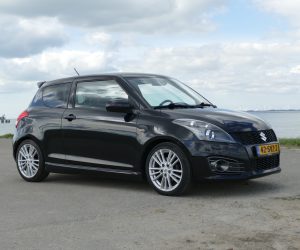 Zwarte Suzuki Swift Sport geparkeerd aan het water, voorzien van sportieve velgen en aerodynamische details.